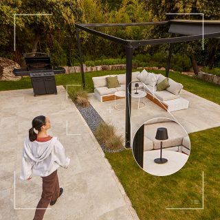 A person walks on a patio near outdoor seating with a color changing table lamp, highlighting smart lighting in a garden setting.