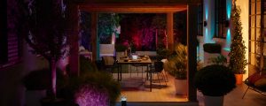 Outdoor patio dining area illuminated by vibrant smart lighting in purple, blue, and orange hues, creating a colorful evening ambiance.