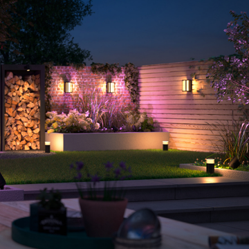 Outdoor backyard scene at dusk with LED light panels and wall lights casting a soft ambient glow over garden and patio areas.