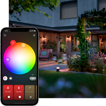 A smartphone displays a color wheel lighting control app set to 75% brightness in front of an illuminated backyard patio.