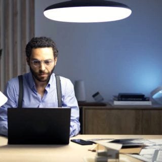 Person working at a desk with bright overhead lighting, using a laptop in a modern office setting with documents and books.