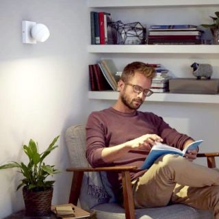 Person reading a book in a living room chair with focused wall lighting illuminating the reading area and bookshelves in the background.