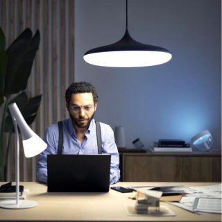 Person working at a desk on a laptop in a modern office, illuminated by bright overhead and desk lighting for focused productivity.