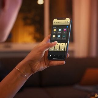 Person adjusting smart lighting settings for the living room on a mobile app, seated in a softly lit indoor environment.