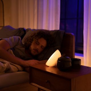 Person resting in bed with a smart light on a bedside table casting a warm glow, creating a cozy bedroom setting at night.