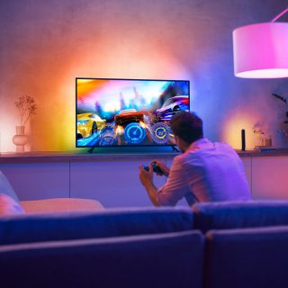 Person playing a video game in a living room with colorful ambient lighting synced to the TV screen, enhancing the gaming experience.