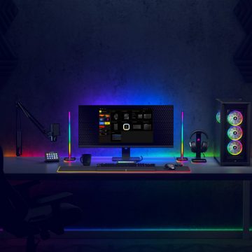 A collection of vertical smart light bars and LED strips placed behind a computer monitor and desk, emitting multicolor lighting for workspace.