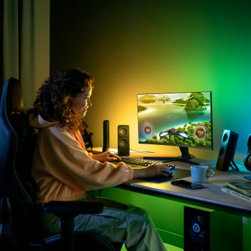 Person gaming at a desk in a home setting, with colorful smart lighting illuminating the wall behind the monitor.