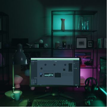 LED light strips installed on shelves behind a computer monitor emit green and pink light, illuminating objects and workspace.