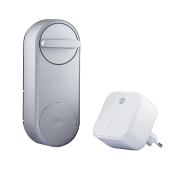 Silver smart door lock with a matte finish and circular turn knob, shown next to a compact white plug-in device.