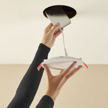 Hands installing a round white smart ceiling light panel and connecting its control box into a circular ceiling opening.