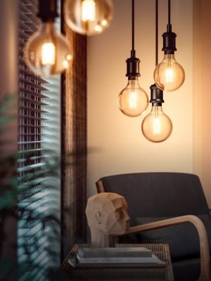 Collection of filament smart bulbs suspended above a chair, emitting warm light onto a nearby table and decorative sculpture.