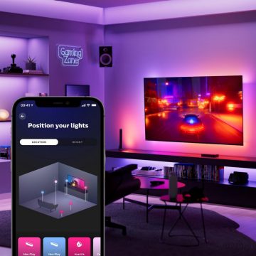 Hue sync app's virtual room set-up screen on mobile device in the foreground. Racing game on hanging TV screen and synced-up lighting in the background.
