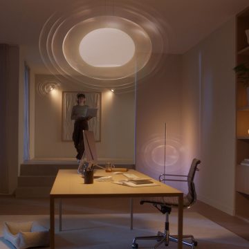 A person stands in a modern home office with smart ceiling lighting illuminating the desk and workspace, supporting focused work.