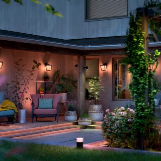 Outdoor smart lighting fixtures installed along garden steps and mounted on walls, illuminating patio seating and surrounding plants.