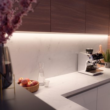 Flexible light strip mounted under wooden kitchen cabinets, casting white illumination onto a marble backsplash and countertop.