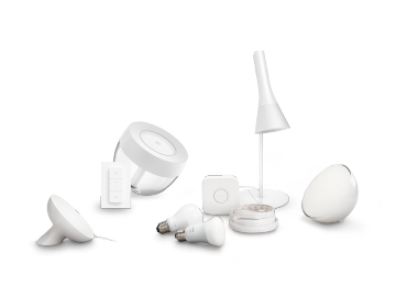 A collection of white smart lighting products including bulbs, lamps, a remote, a light strip, and a motion sensor, all with similar design.