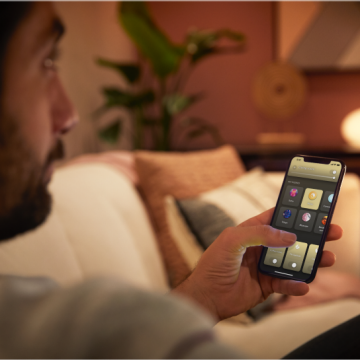 Person on a sofa using a smartphone app to adjust ambient lighting in a modern living room with decorative elements.
