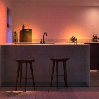 Smart lighting installed under kitchen cabinets illuminates countertop, highlighting sink, stools, and fruit bowl in dining area.