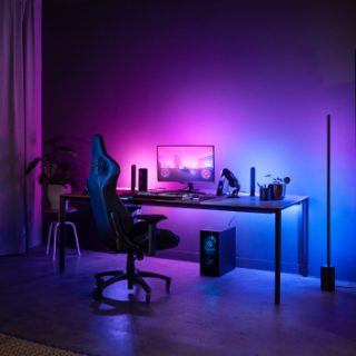 Gaming lighting setup with smart light bars and floor lamp placed around a desk, casting colored illumination on walls and surfaces.