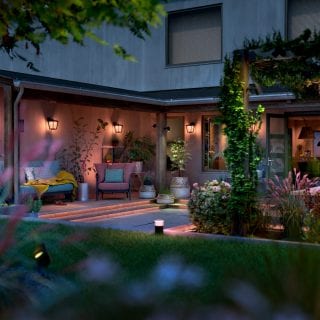 Outdoor smart wall lights and pathway lights are installed around a backyard patio, illuminating seating and plants.