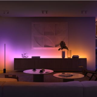 Living room with soft ambient glow from smart lighting behind cabinet, highlighting wall art and furniture with purple and orange hues.