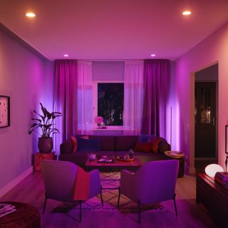 Modern living room illuminated by smart lighting, creating a soft ambient glow with purple and pink tones across furniture and walls.