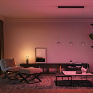 Pendant smart lights with clear glass shades suspended from the ceiling, casting colored illumination onto a living room area.
