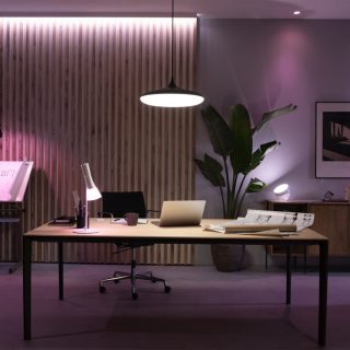 Pendant light fixture above office desk, desk lamp and smart spot light illuminate workspace, highlighting architectural plans.