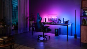 Desk setup with gaming chair, monitor, and smart lighting casting purple and blue light on wall and floor behind the desk.