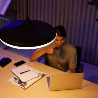 Person working at a home office desk with a pendant light illuminating a laptop, notebook, and coffee mug.