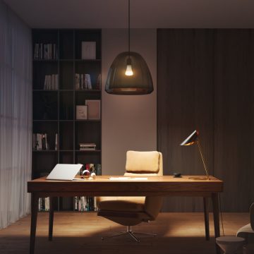 Pendant smart bulb in a translucent shade hanging above a desk, illuminating a home office workspace with shelving in the background.