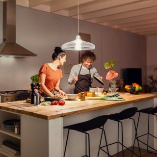 Two people preparing food together in a kitchen, illuminated by a pendant light above the wooden island counter.