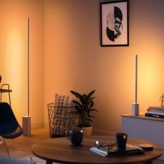 Two slim vertical smart lamps placed near the wall cast warm white light onto the living room, highlighting furniture and decor.