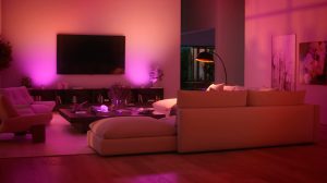 Modern living room with soft pink and purple smart lighting, large sofa, wall-mounted TV, and abstract artwork on the walls.