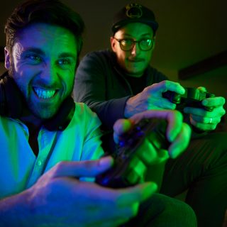Two people playing video games with controllers in a living room, illuminated by colorful green and blue smart lighting.