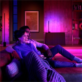 A group relaxing on a living room sofa with smart floor lamps casting purple and pink light, enhancing a cozy evening setting.