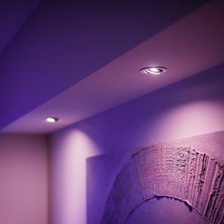 Ceiling-mounted recessed living room light fixtures emitting purple-toned light, illuminating a textured wall art below.