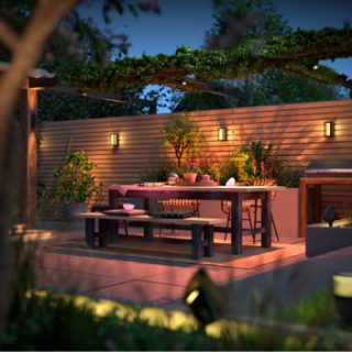A collection of smart outdoor wall lights and spotlights installed around a patio dining area, illuminating the table and seating.