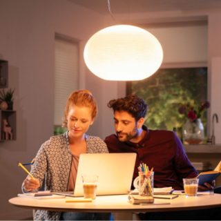 Two people working together at a table with a glowing pendant light above, providing focused illumination in a home setting.