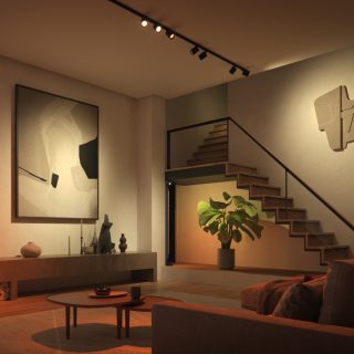 Black track smart light kit mounted on ceiling, illuminating a staircase, wall art, and large plant in a modern living room.
