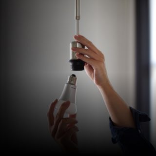 Hands installing a white smart LED bulb into a ceiling light socket, demonstrating setup of smart lighting solutions.