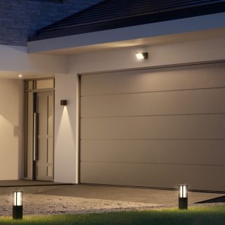 Una puerta principal y un camino de entrada iluminados con lámparas de pedestal, apliques murales y un foco que brilla con una luz blanca brillante e inteligente