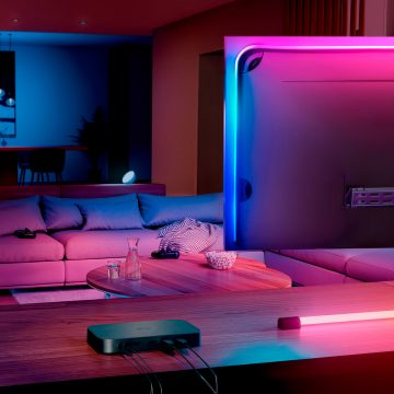 Le boîtier de synchronisation hue 8K se trouve sur une console à côté d'un écran de télévision dans un salon.