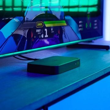 Un boîtier de synchronisation HDMI 8K se trouve sur un meuble de télévision dans une pièce éclairée par une lumière bleue de divertissement.