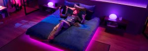 Personne en train d'écouter de la musique sur un lit dans une chambre, entourée de lumières LED colorées qui se synchronisent avec la musique dans des tons de rose, violet et bleu.