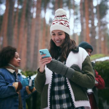 Una donna sorridente controlla il suo sistema di sicurezza domestica intelligente sullo smartphone mentre si trova in una foresta