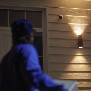Persona addetta alle consegne si avvicina alla porta d'ingresso dove è installata la videocamera Philips Hue Secure