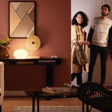 Philips Hue 스마트 전등이 따뜻한 백색 스마트 조명으로 환하게 밝히고 있는 거실로 커플이 들어섭니다.