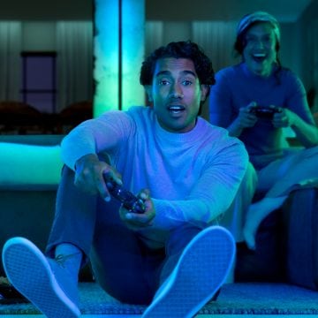 Een gamer die een game speelt op een gamingopstelling met drie beeldschermen, Hue gradient lightstrips en tafellampen. 